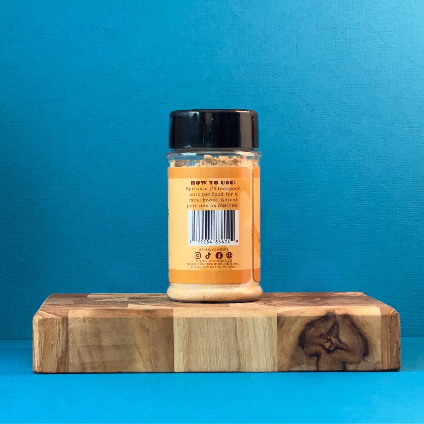 Jar of peanut butter powder on a wooden block with a blue background